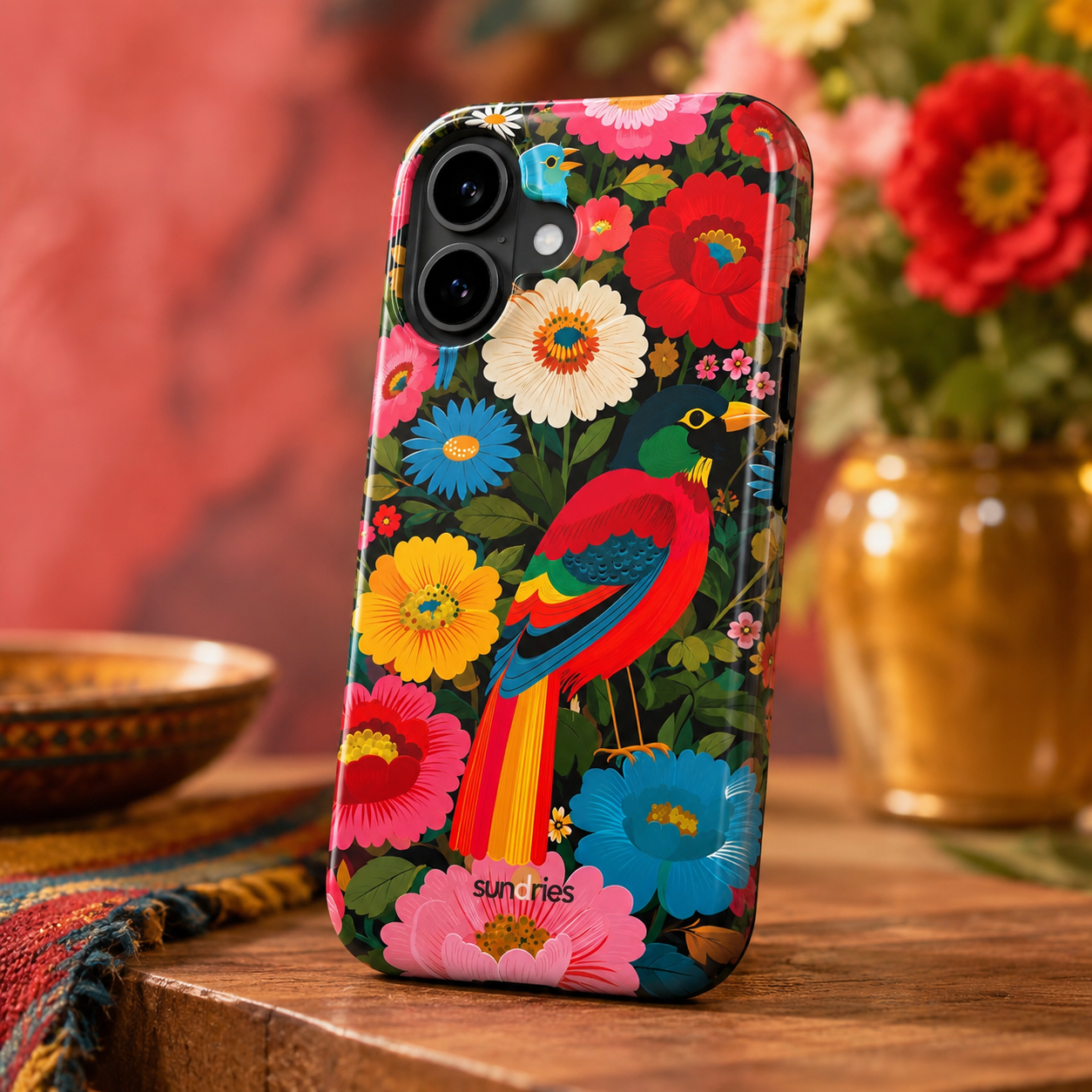 Phone case with colorful floral and bird design on a wooden surface with flowers in the background