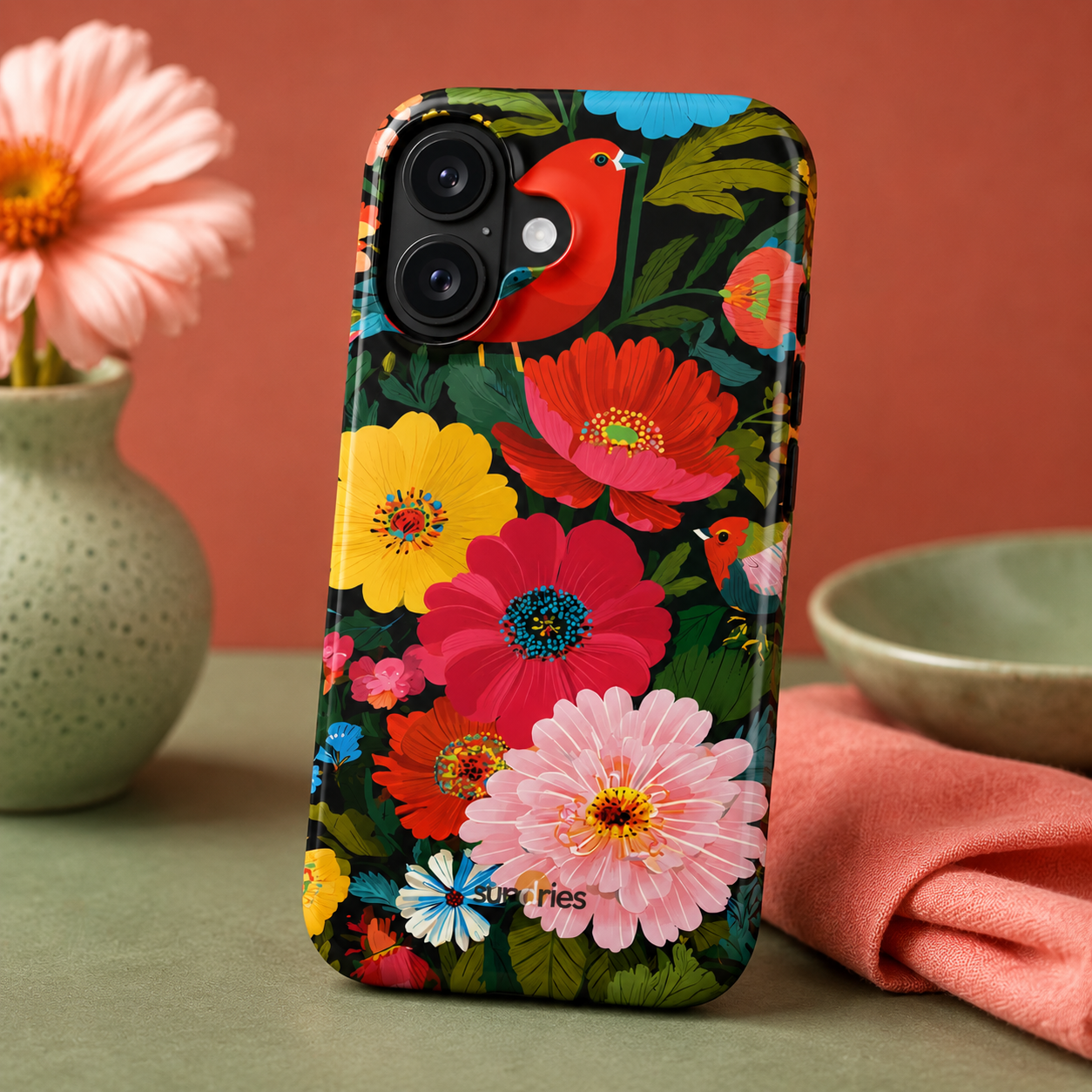 Phone case with colorful floral design on a table with flowers and a bowl.