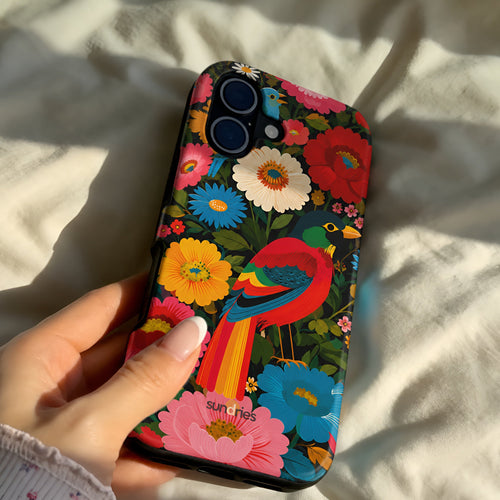 Colorful floral and bird phone case held by a hand on a light fabric background