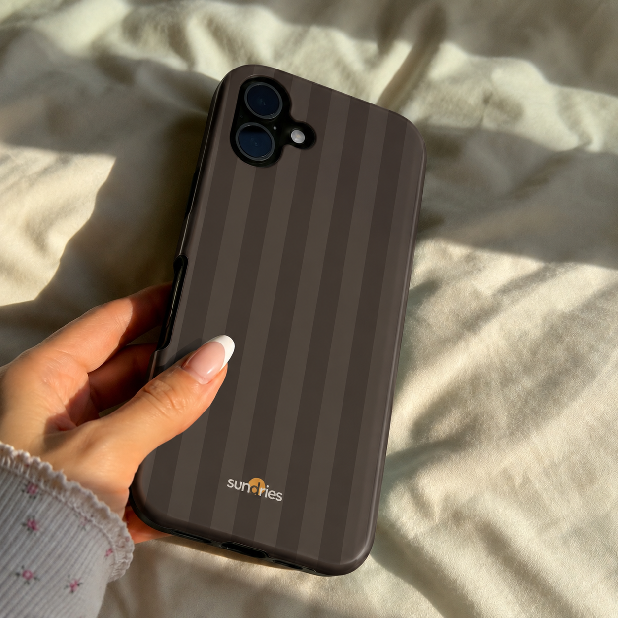 Hand holding a phone with a striped case on a light fabric background