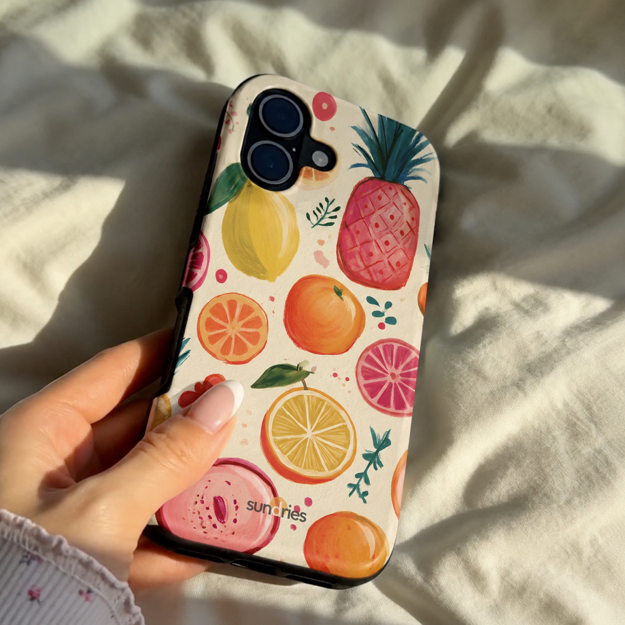 Phone case with fruit pattern held by a hand on a light fabric background