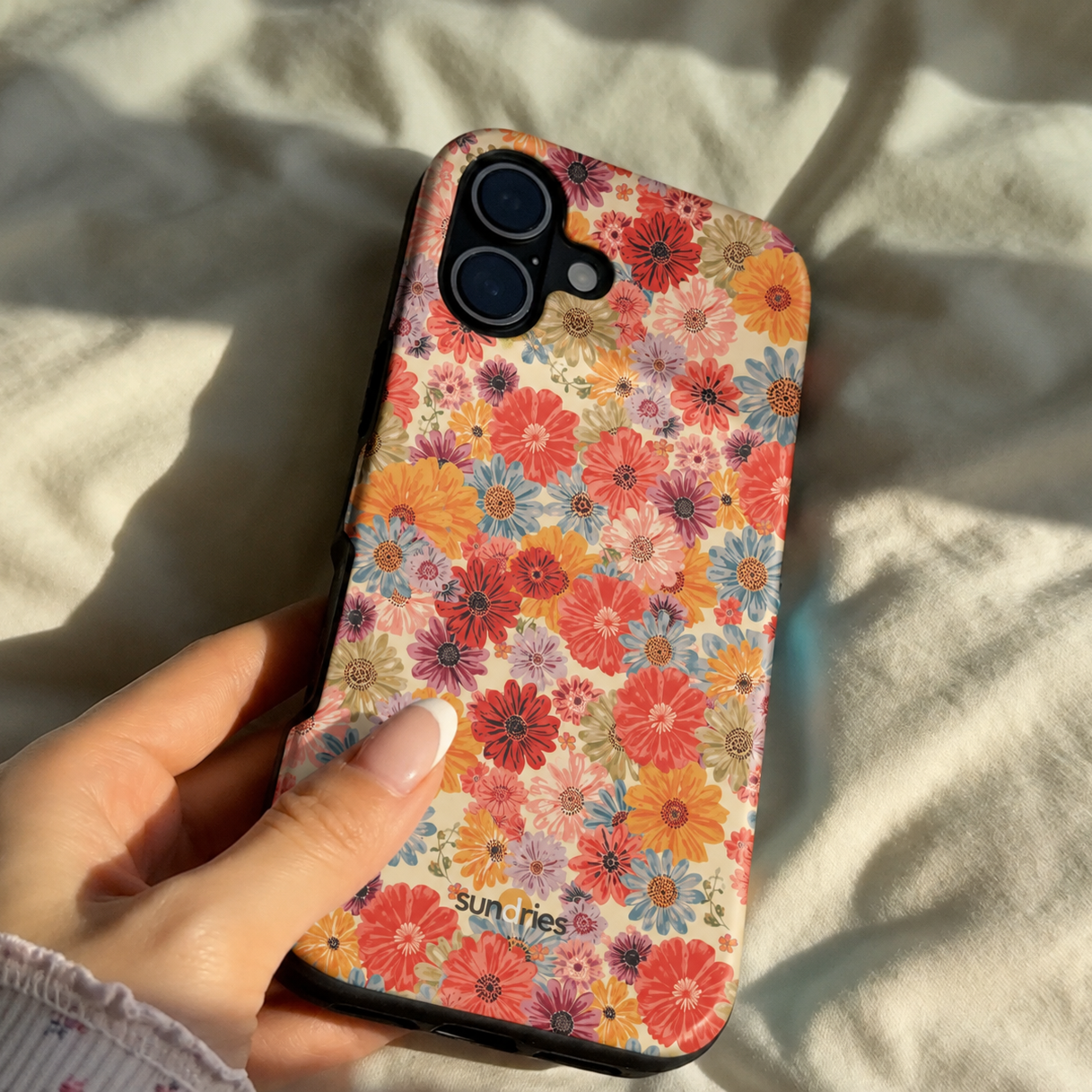 Floral patterned phone case held by a hand on a light fabric background
