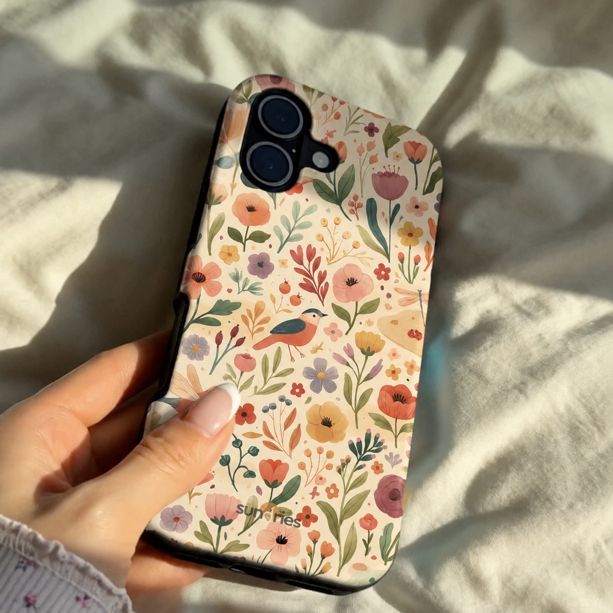 Phone case with floral pattern held by a hand on a light fabric background