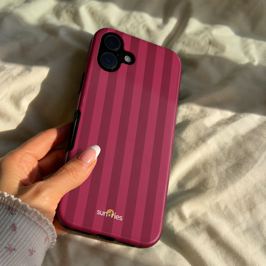 Hand holding a pink striped phone case with 'sun rifles' branding on a light fabric background
