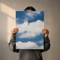 Person holding a poster of a blue sky with clouds and an airplane.