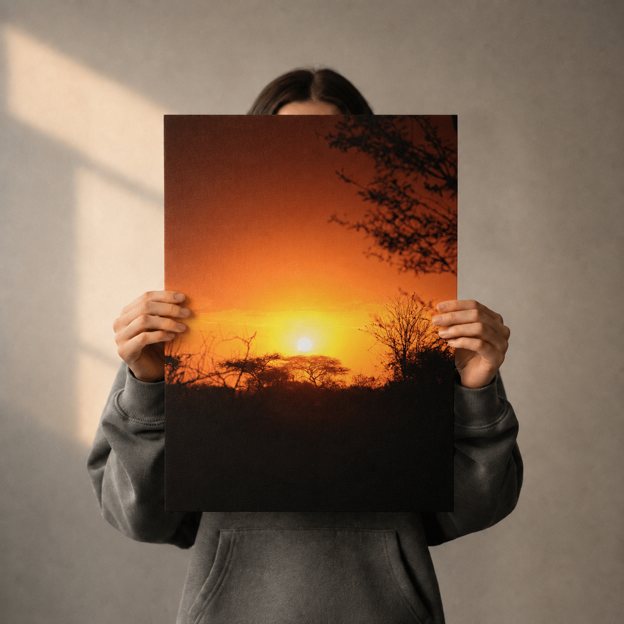 Person holding a poster of a sunset over a field against a plain background